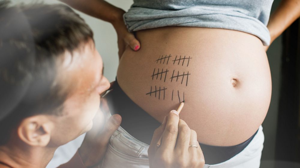 Husband writing counting weeks on prepregnancy wife's belly
