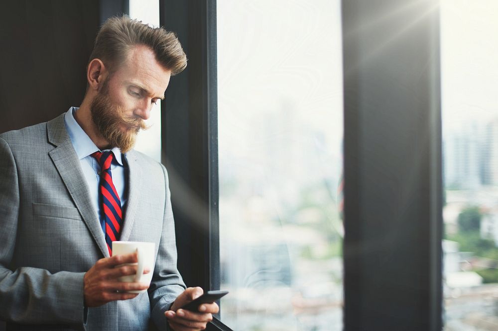 Businessman using a phone and drinking coffee