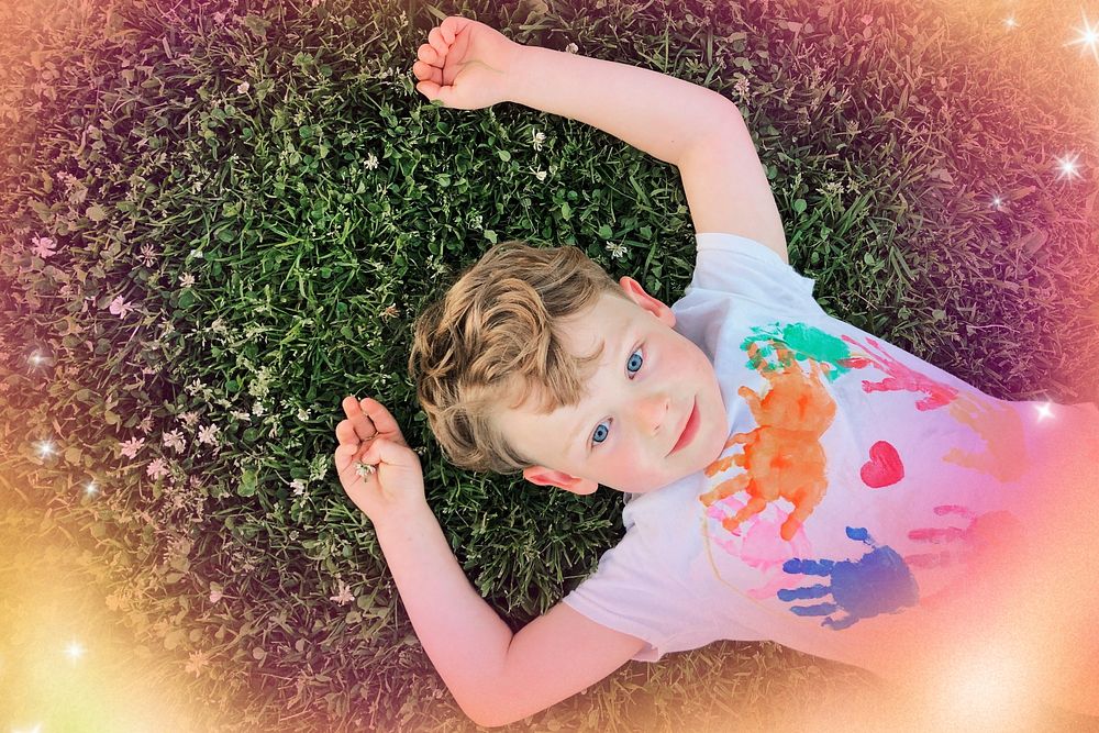 Smiling kindergarten boy lying down on the grass aerial view