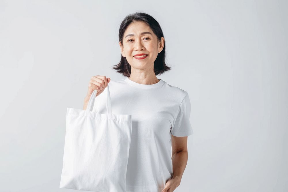 Asian woman in 60s in white tee holding a white tote bag mock up accessories accessory clothing.