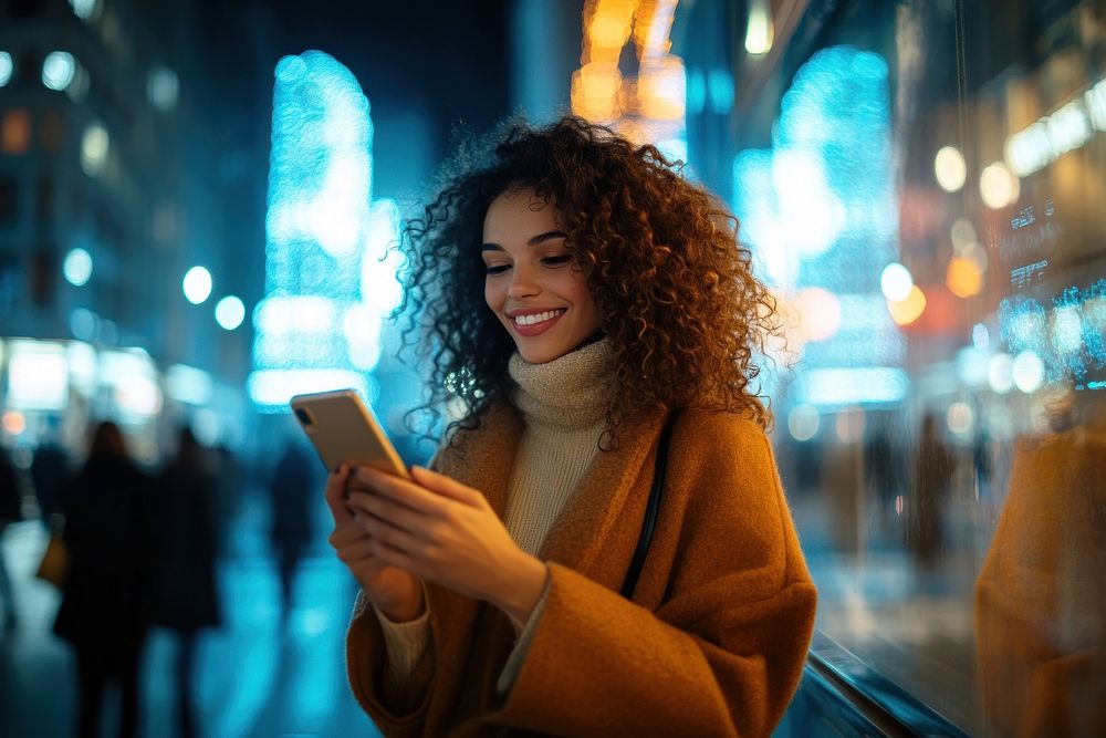 Young woman with curly hair uses her mobile phone background smiling setting.