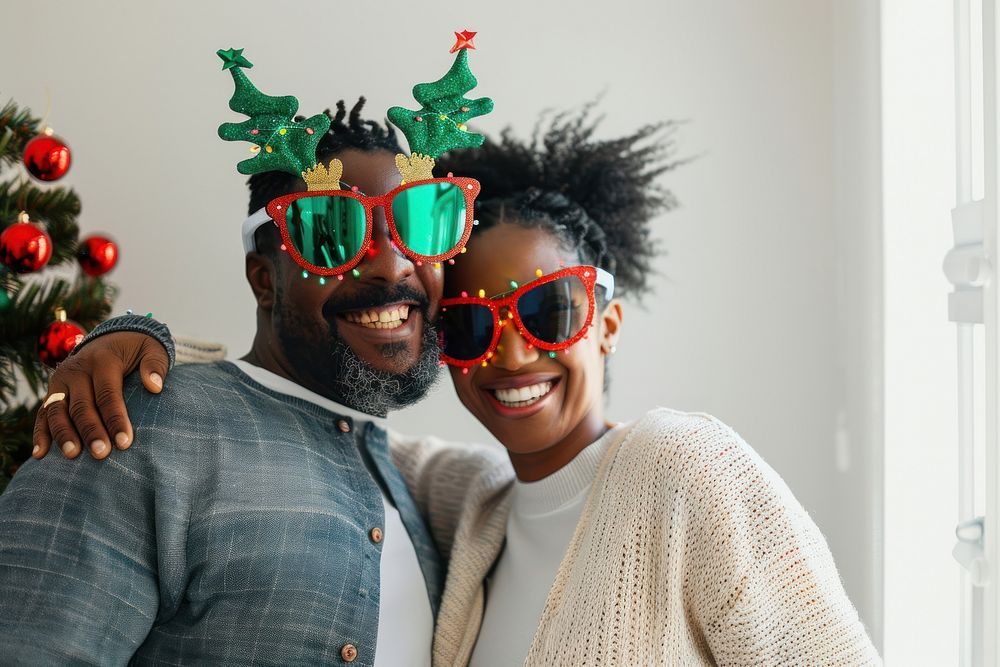 A Happy black couple wearing cute Christmas tree glasses and reindeer antlers glasses celebrating together on a white room…