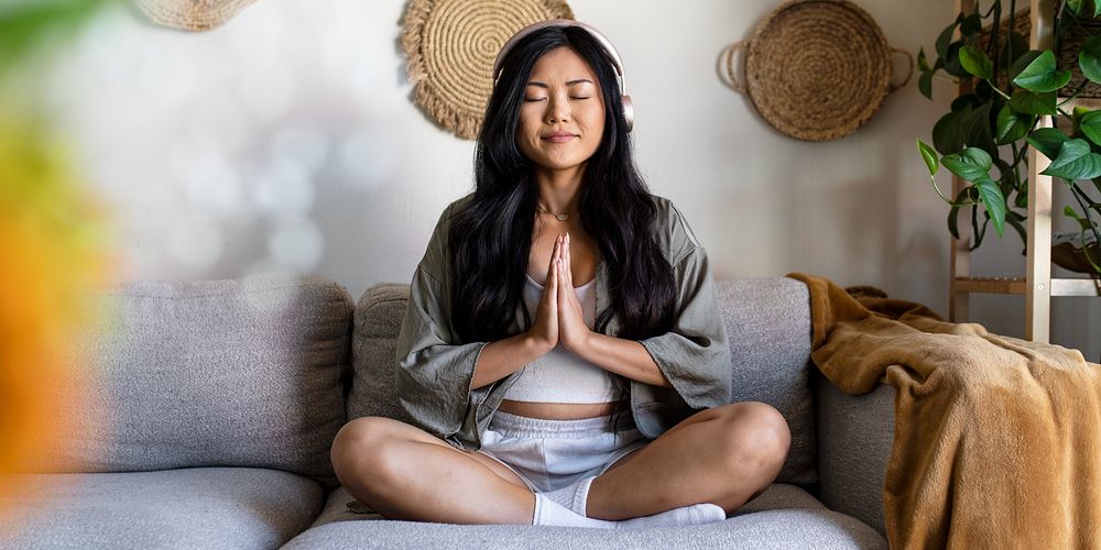 Peaceful Asian woman meditating on sofa