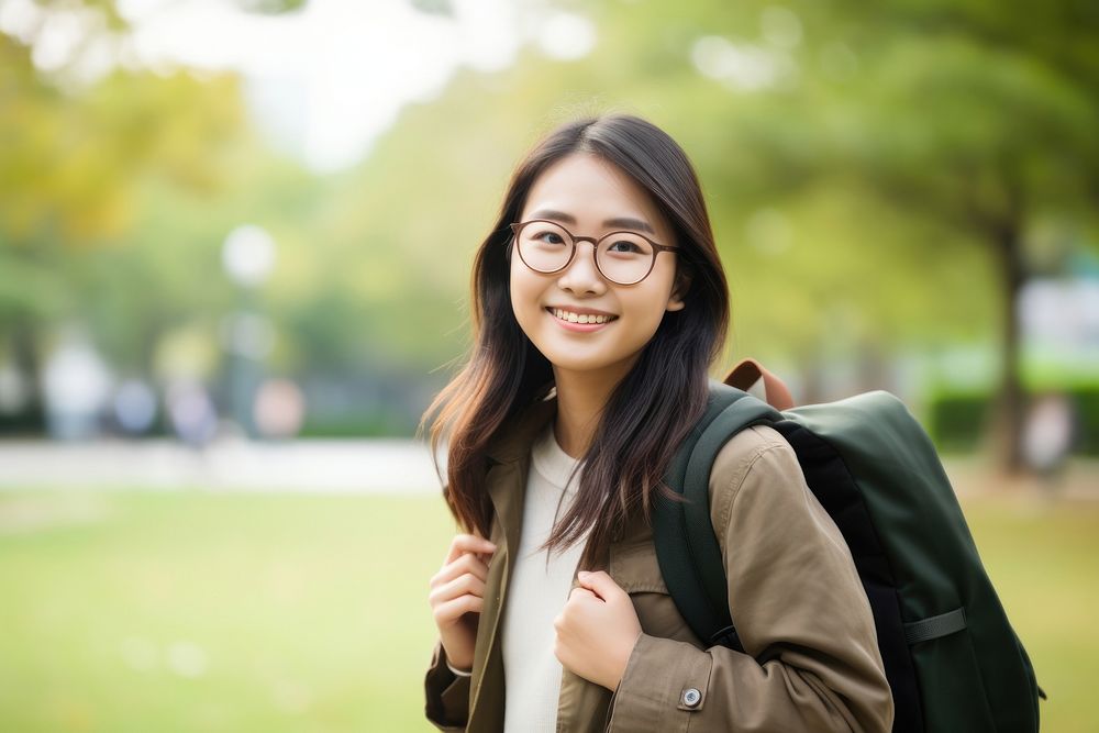 Smiling young chinese woman student wearing glasses and casual background clothing backpack.