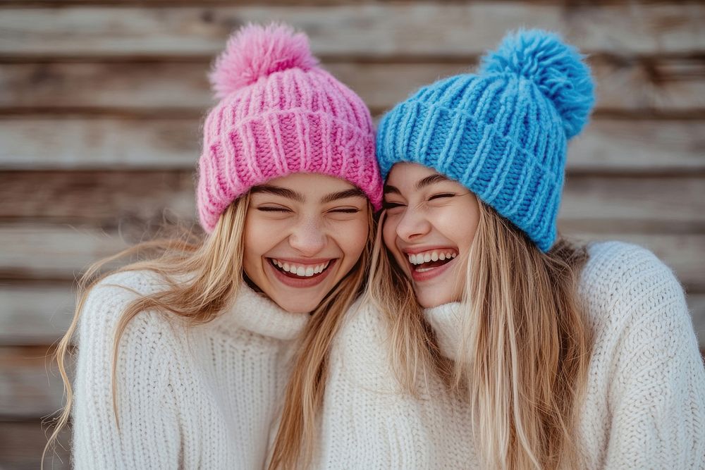 A happy friends with knitted pink hat hugging girl friend with blue knitted hat sweaters background laughing.