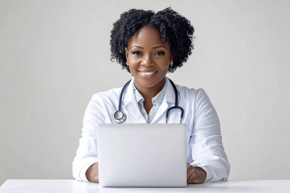 Happy mature black female doctor looking young and smart using laptop looking at camera white professional electronics.