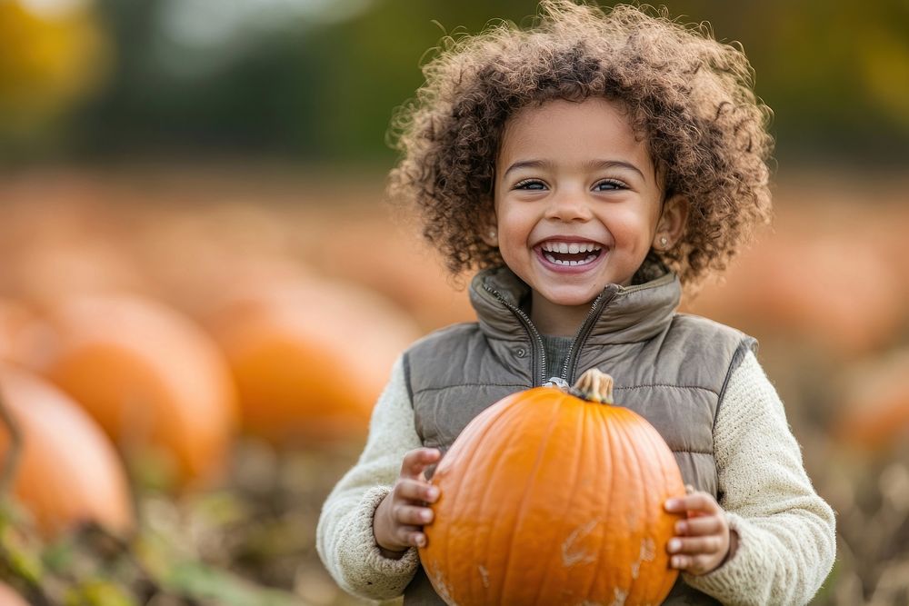 Child holding pumpkins hair outdoors smiling.