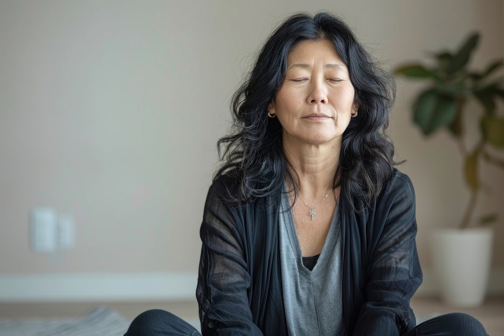 Middle aged asian woman sitting on the floor at home with eyes closed meditation accessories mindfulness.