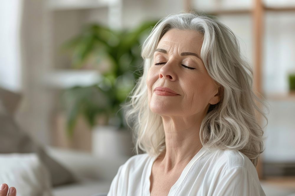 Smiling Middle aged woman meditating at home with eyes closed white hair mindfulness.