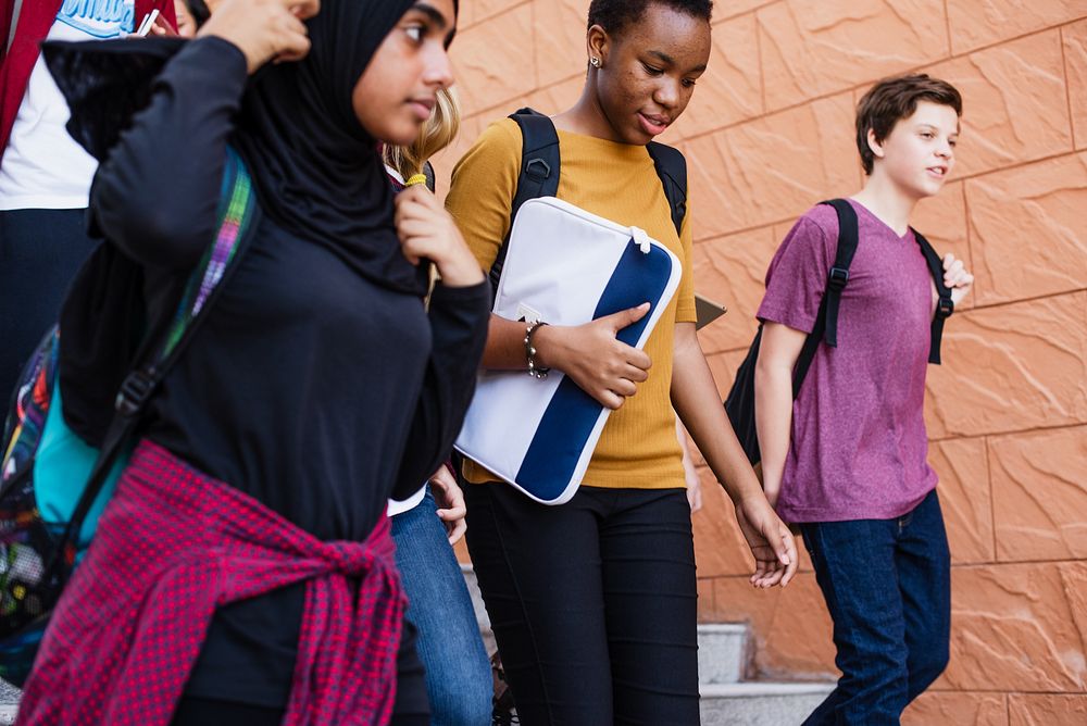 Diverse group of students, including a young woman in a hijab, a Black girl walking together. Students carrying backpacks…