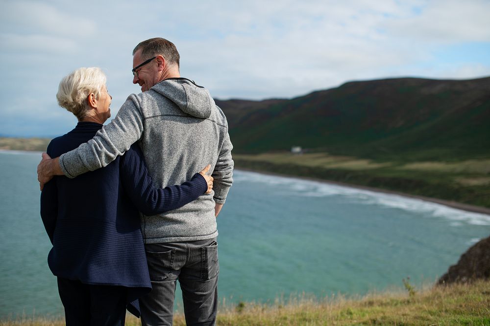 Elderly Caucasian couple, man and woman, embracing by the coast. The elderly couple enjoys the scenic view, man and woman…