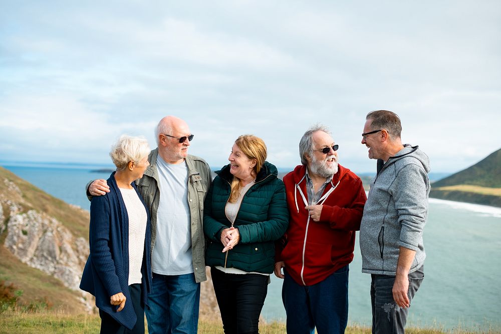 Group of elderly friends, men and women, stand together by the coast. Senior friends embrace, Elderly friends share moments…