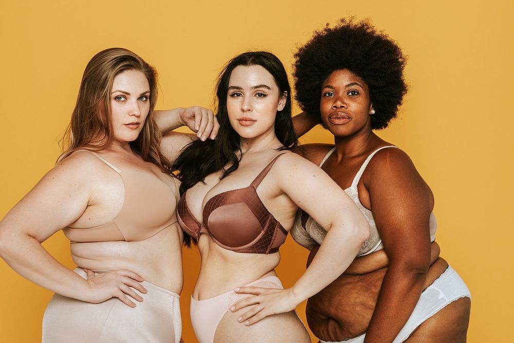 Three confident plus size diverse women in lingerie, showcasing body positivity against yellow background. Diverse women and…