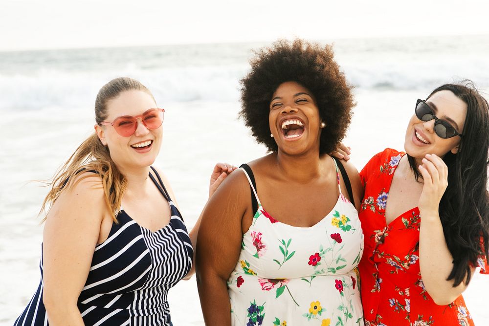 Diverse women friends enjoy beach in summer holidays. Diverse plus size women laugh and smile in summer dresses at beach.…