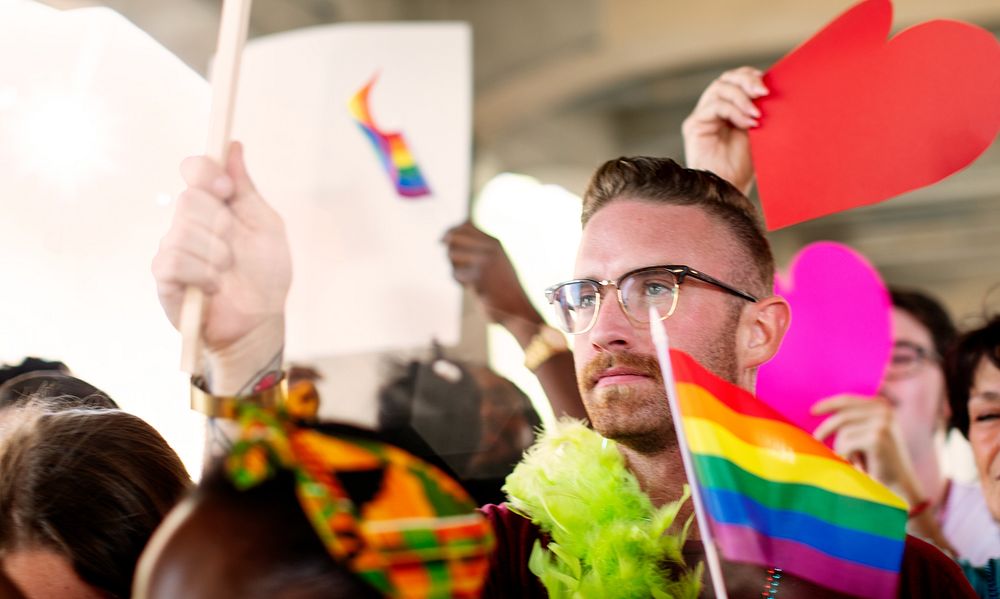 A diverse group of LGBTQ people at a pride parade. LGBTQ man with rainbow flag. LGBTQ man in pride parade, pride month…