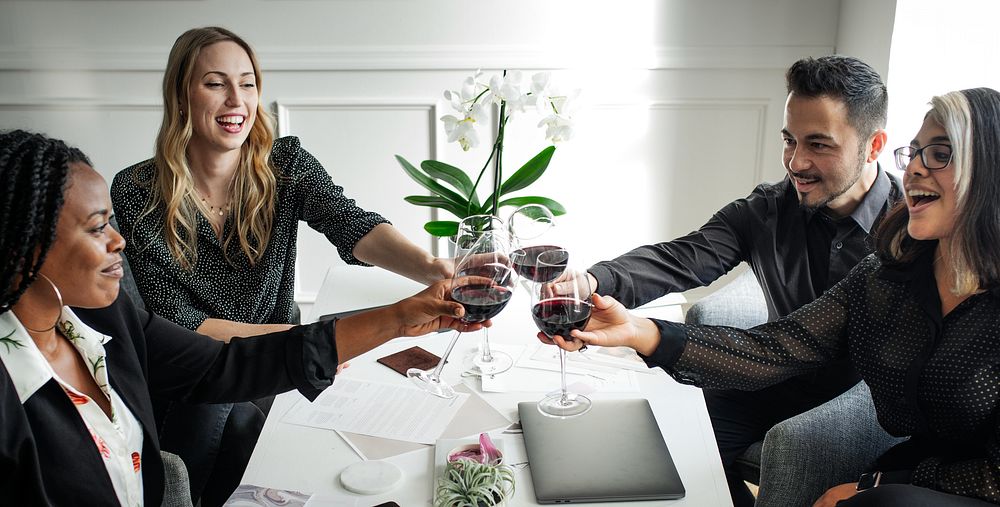 A diverse business group of four friends celebrate with red wine for achievement. Diverse business people enjoy a joyful…