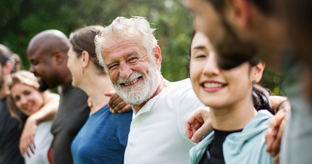 Elderly man and diverse people hugging each other. Diverse group of women and men embrace each other at park. Unity and…