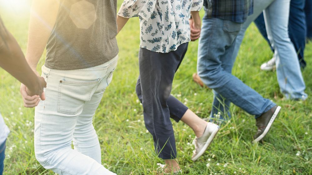 Group of diverse people walking holding hand on grass. Diverse group of men and women walking together at park. People…