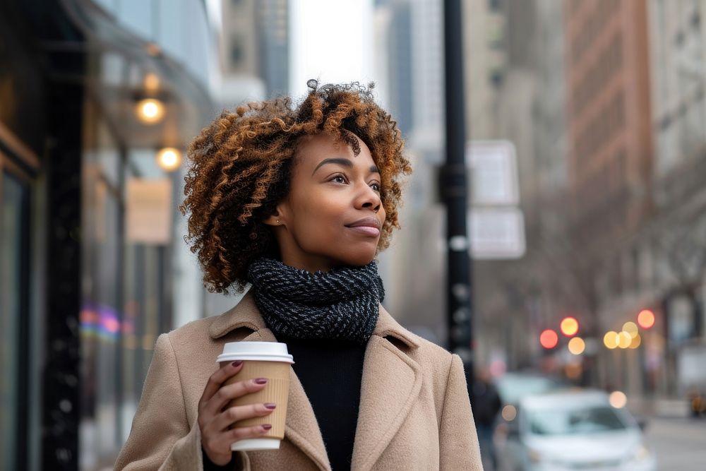 An african american woman walking with a coffee on a city sidewalk scarf cup mug.
