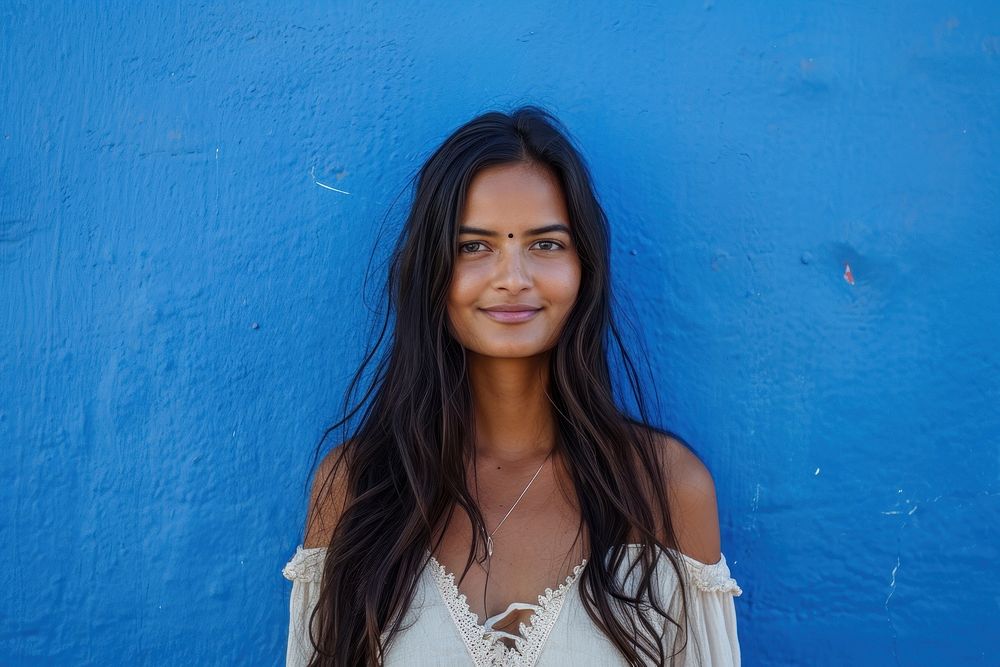 Indian american woman smile blue wall.