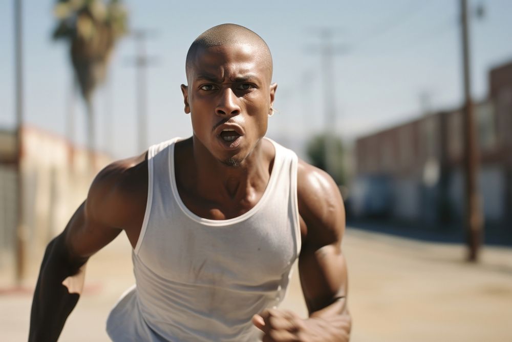 Black man buzz cut hair wearing white tank top and blue jean running adult determination.