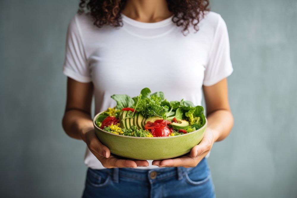 Woman in t-shirt and jeans standing and holding vegan superbowl or salad bowl food midsection vegetable. AI generated Image…