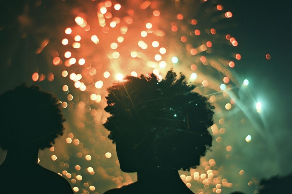 Fireworks with silhouettes of black people light outdoors night.