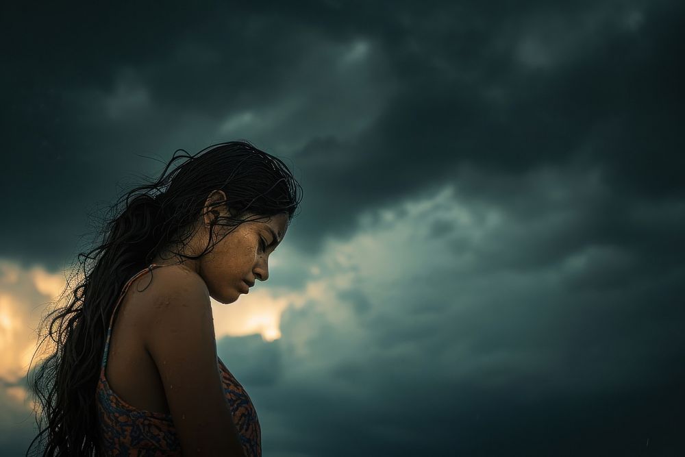 A Latina Mexican woman stands with her head bowed darkness portrait outdoors.
