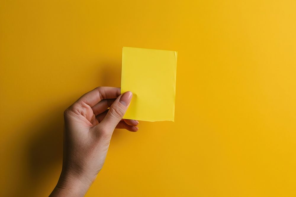 Hand holding blank yellow sticky note paper yellow background activity. AI generated Image by rawpixel.