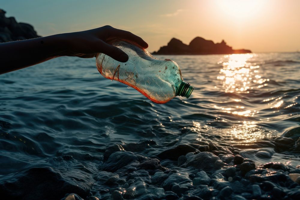 Hand picking up an empty plastic bottle form the sea outdoors nature ocean. AI generated Image by rawpixel.