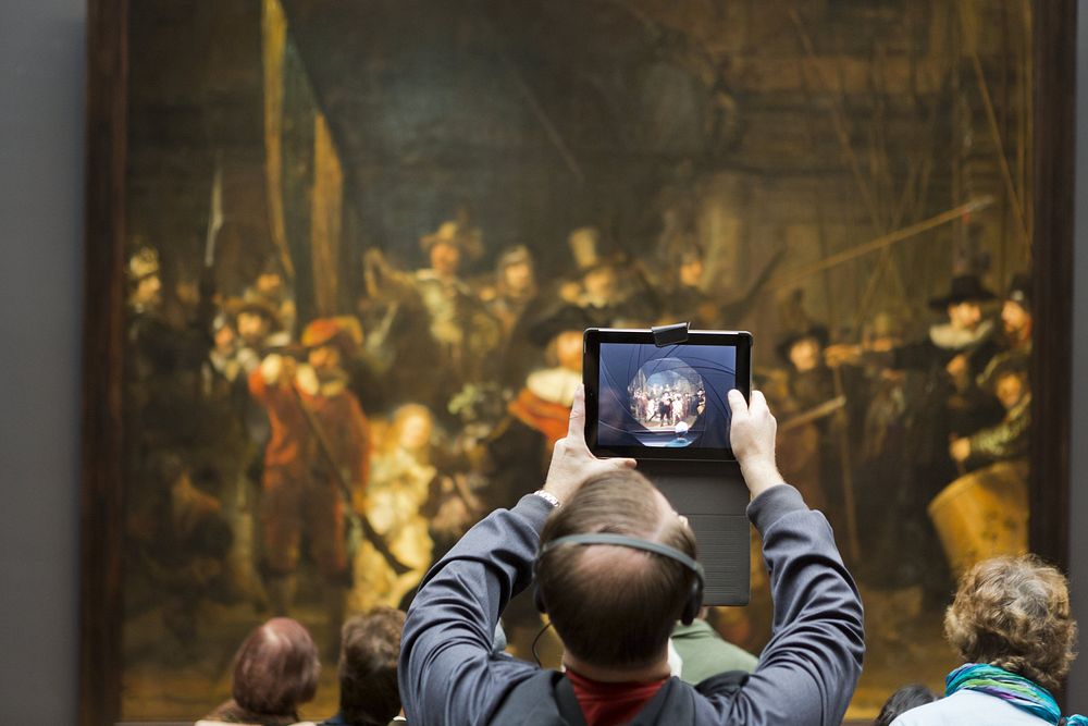 Museumbezoeker met een audiotour neemt een foto met een tablet van de Nachtwacht in de Nachtwachtzaal (2013) by René den…