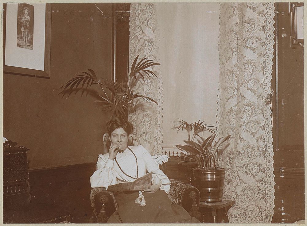 Vrouw met een tijdschrift zittend in de hoek van een kamer (c. 1900 - c. 1910) by anonymous