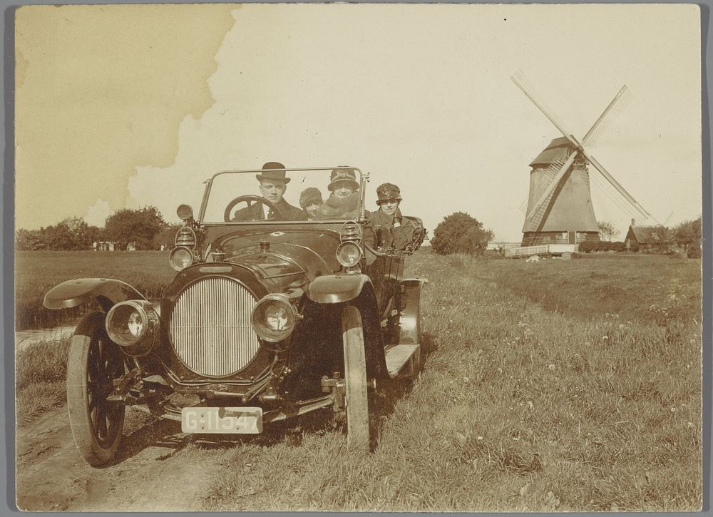 Groep passagiers in een auto met op de achtergrond de Voorste Molen in Kortenhoef (c. 1920 - c. 1935) by anonymous