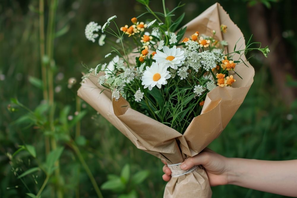 Hand holding bouquet wrapped in craft paper outdoors flower plant.