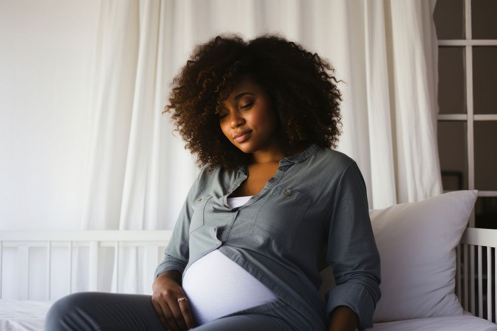 Pregnant black woman touching her belly while sitting on her bed adult contemplation anticipation. AI generated Image by…