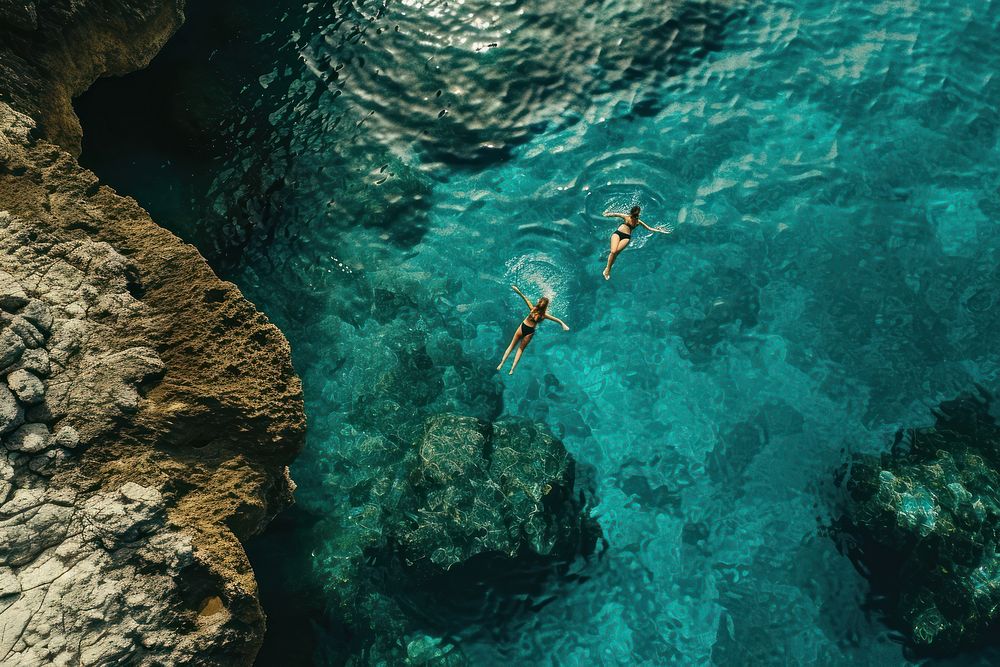 Two people falling below a cliff over the ocean swimming outdoors nature.