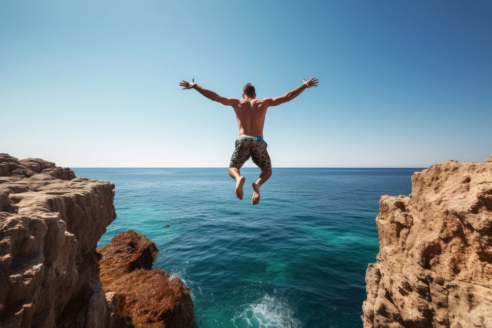 Athletic young man jumping off a rocky diving cliff outdoors.