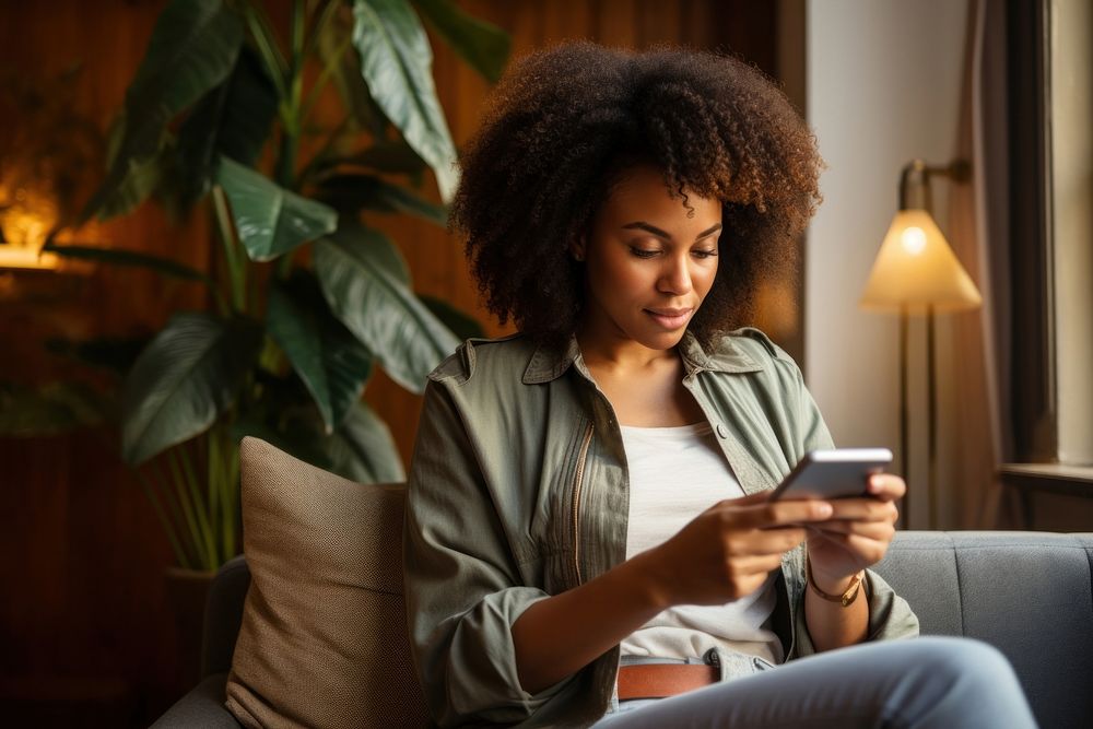 Young Black woman managing online banking with smartphone sitting on the sofa adult head portability.