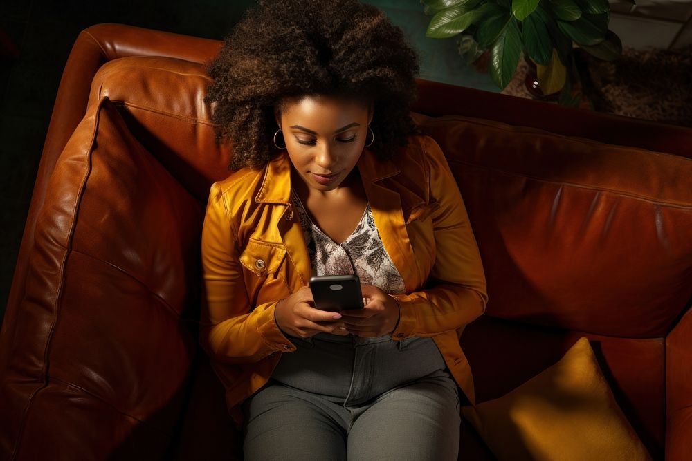 Young Black woman managing online banking with smartphone sitting on the sofa furniture portrait adult.