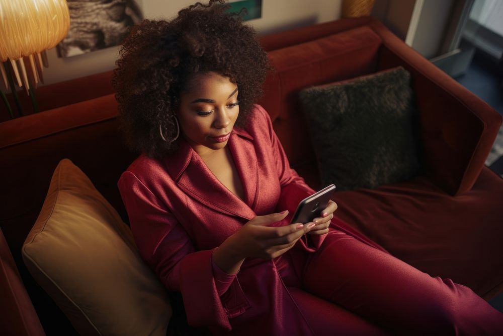 Young Black woman managing online banking with smartphone sitting on the sofa adult head electronics.