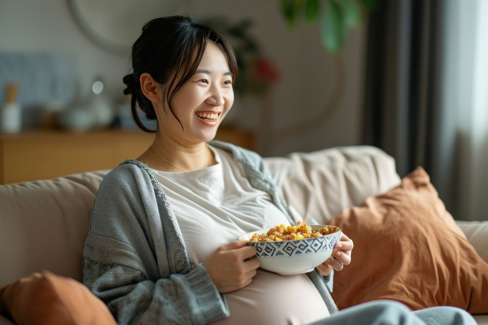 Pregnant chinese woman smiling sitting eating.