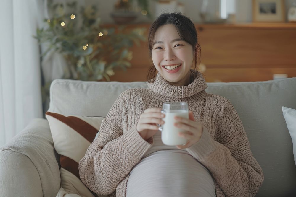 Pregnant korean woman drinking smiling sitting.