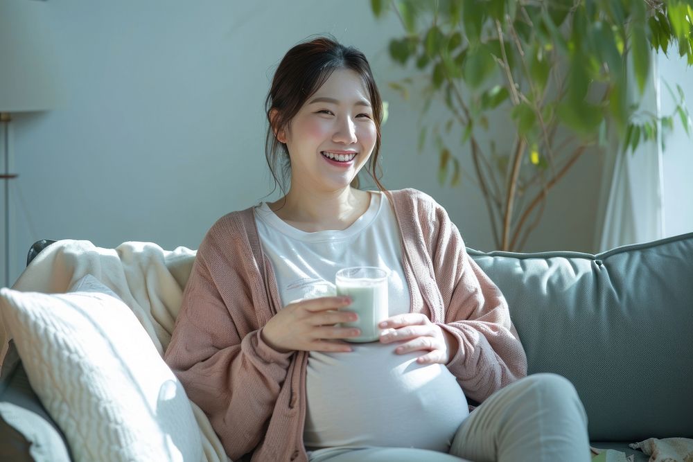 Pregnant korean woman sitting drinking smiling.