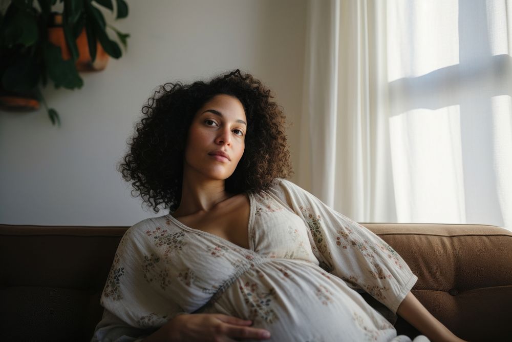 A mixed race pregnant woman adult sofa contemplation.