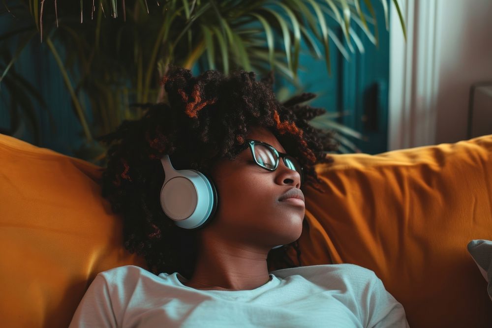 Photo of black person listening music on sofa headphones headset electronics.