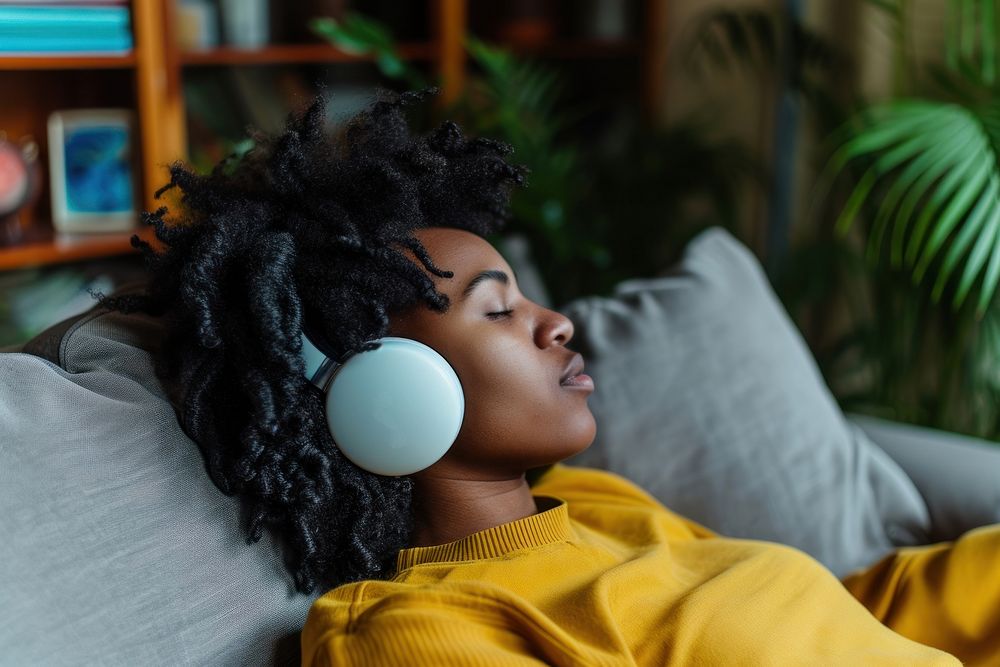 Photo of black person listening music on sofa headphones relaxation technology.