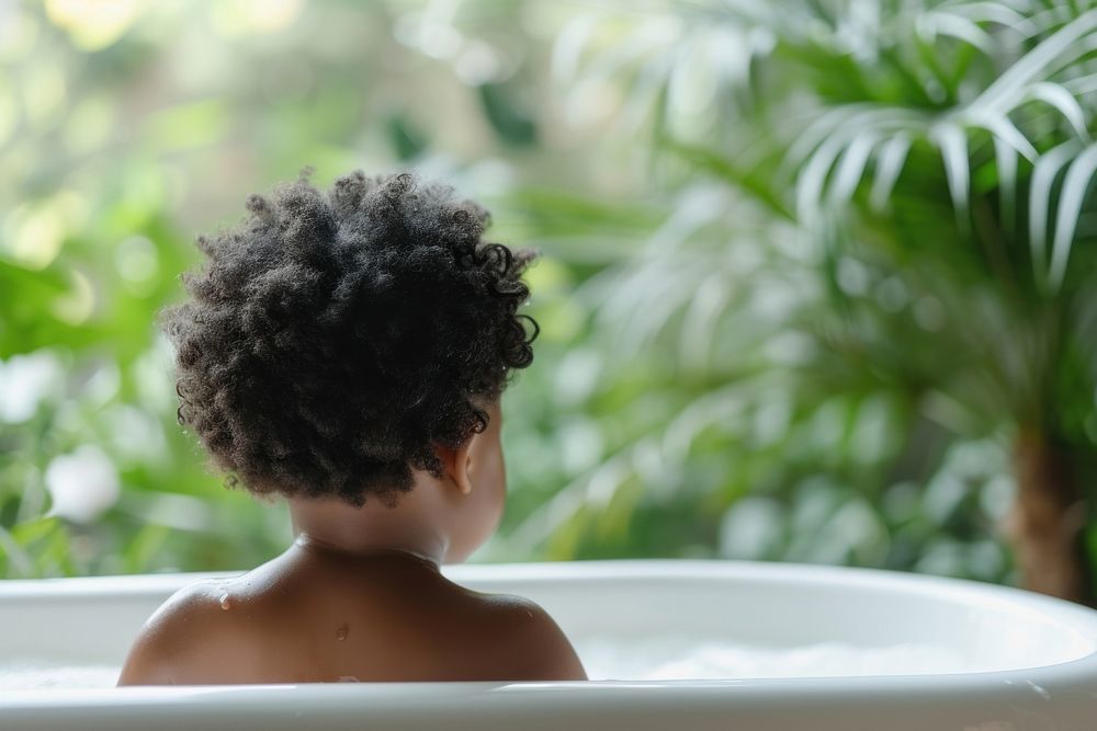 Photo of little black kid in large tub bathtub back relaxation.