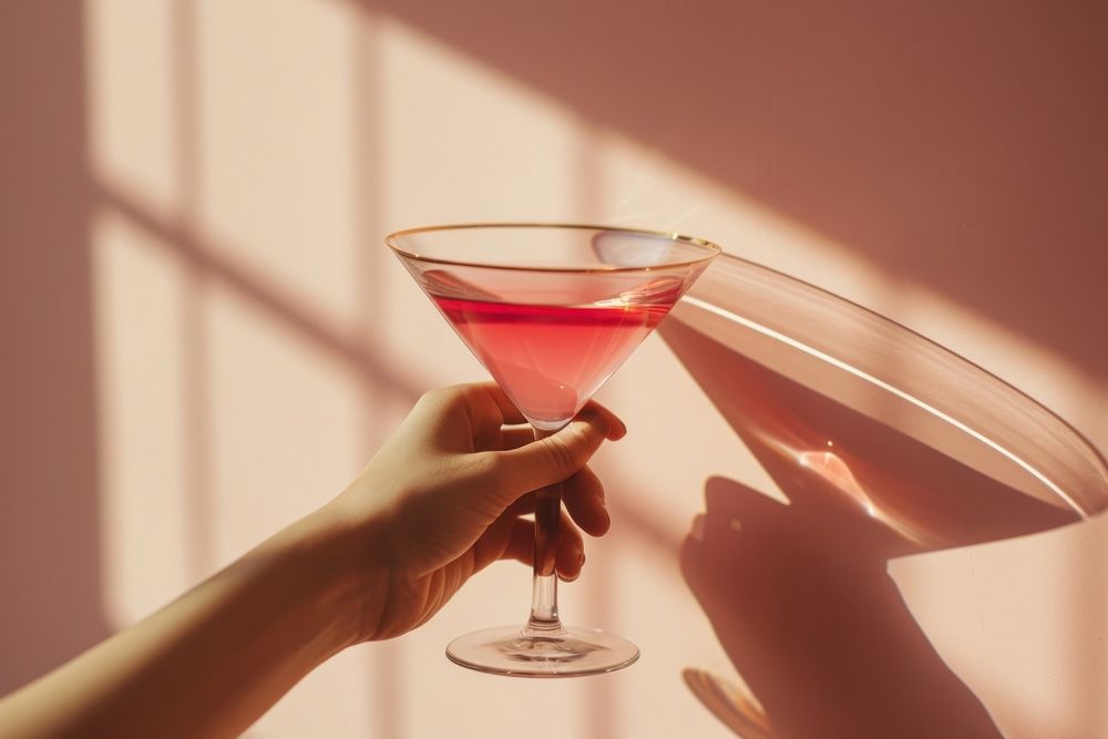 Hand holding cocktail glass martini drink pink.