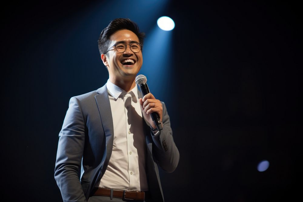 Asian man speaker on professional stage microphone smiling glasses.