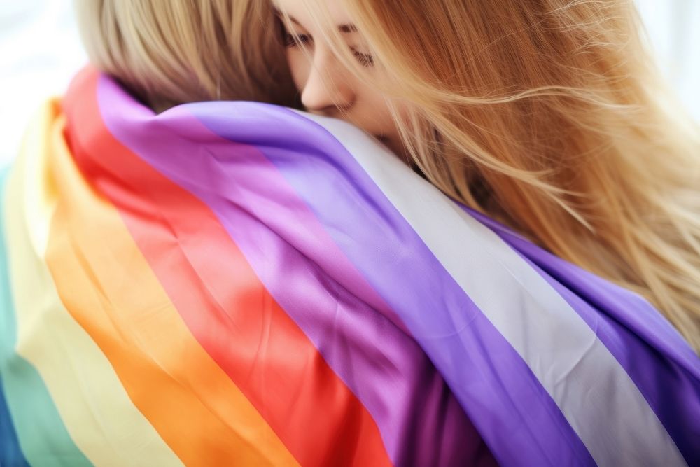 Cute gay sweethearts embracing wrapped in rainbow flag purple togetherness affectionate.